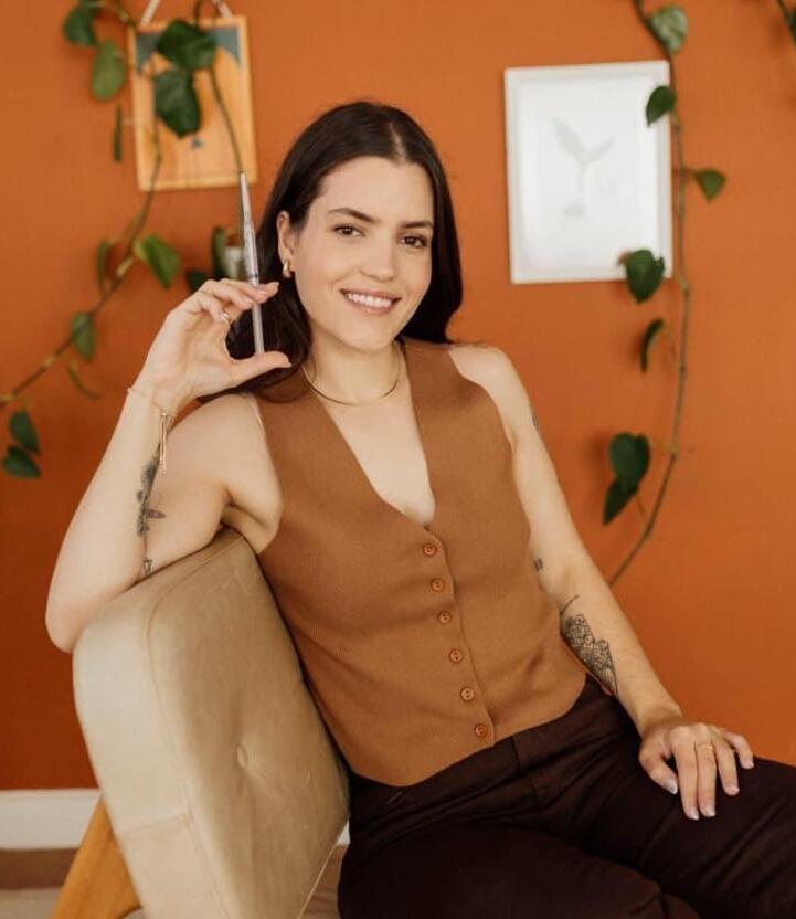 Enfermeira Giovana Braga em consultório, segurando uma caneta, sorrindo